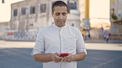 Young hispanic man using smartphone at street