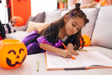 Adorable hispanic girl drawing on notebook having halloween party at home
