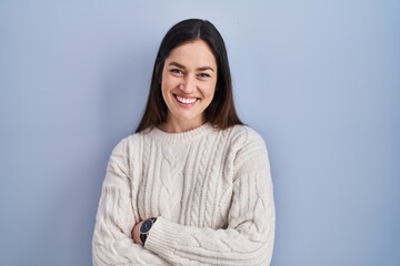 Young brunette woman standing over blue background happy face smiling with crossed arms looking at the camera. positive person.