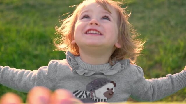 Girl on a swing. Little 2 years child swinging in summer at sunset. Slow motion of beautiful baby sitting on a swing in a park, sunny evening. Smiling young kid enjoying the rope seesaw at playground.