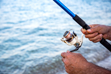 Man's hand holds fishing rod on a blue sea or lake background