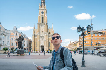 Man tourist with sightseeing map standing outdoors in the old town. Portrait of handsome male traveler backpacker in sunglasses holding map and looking for attractions
