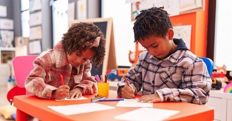 Adorable african american boy and girl preschool students sitting on table drawing on paper at kindergarten