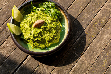 Coriander chutney in a bowl with spring of cilantro, lime wedges and one Brazil nut on top.