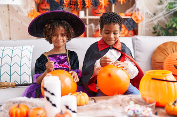 Fototapeta premium Adorable african american boy and girl having halloween party drawing on balloon at home