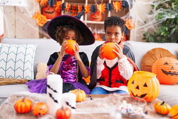 Adorable african american boy and girl having halloween party inflating balloon at home