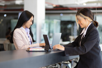 Businesswoman secretary colleague working with laptop in office. Two receptionists work at the counter.