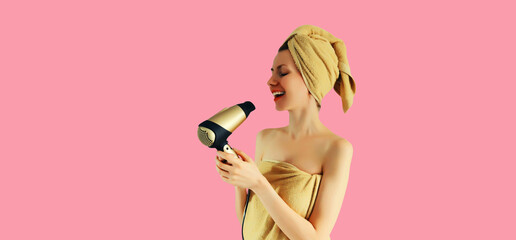 Portrait of happy smiling young woman drying wet hair in wrapped bath towel after taking a shower on pink background
