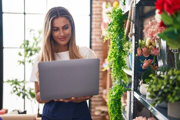 Young blonde woman florist smiling confident using laptop at florist