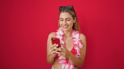 Young blonde woman tourist using smartphone smiling over isolated red background