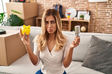 Young blonde woman holding led bulb and piggy bank depressed and worry for distress, crying angry...