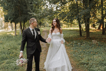 the bride and groom hold hands, walk in the garden looking at each other