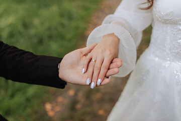close-up photo, groom holding bride's hand, gold ring on finger, tenderness in photo, blurred background