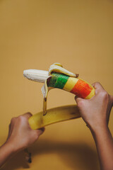 Peel off banana painted in LGBT flag colors on yellow background. Sex concept. Symbol