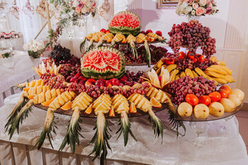table with various fruit decorations. Watermelon carving, pineapple slices, grapes, orange