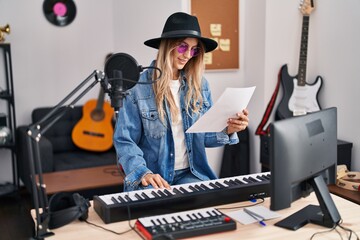 Fototapeta na wymiar Young woman musician smiling confident playing piano keyboard at music studio