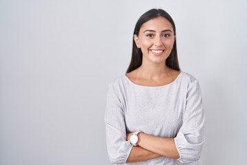 Young hispanic woman standing over white background happy face smiling with crossed arms looking at the camera. positive person.