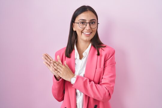 Young hispanic woman wearing business clothes and glasses clapping and applauding happy and joyful, smiling proud hands together