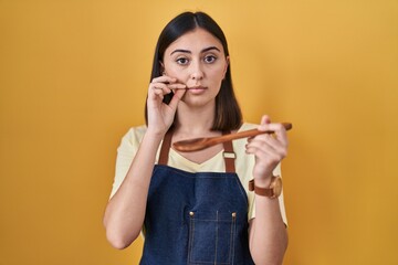Hispanic girl eating healthy  wooden spoon mouth and lips shut as zip with fingers. secret and...
