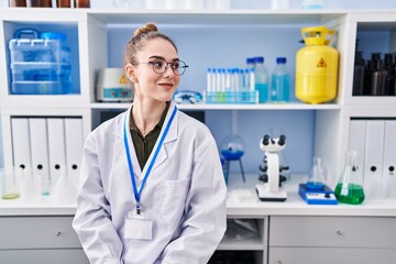 Young hispanic girl working at scientist laboratory looking to side, relax profile pose with...