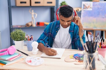 Fototapeta premium Young latin man artist listening to music drawing on notebook at art studio