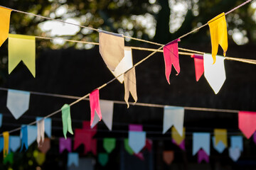 Close em diversas bandeirinhas coloridas em decoração de festa junina com fundo escuro desfocado.