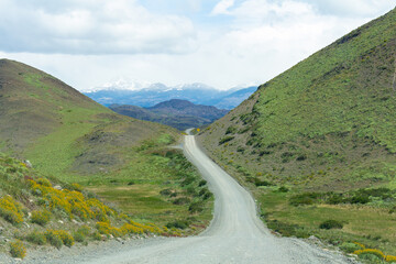 Estrada de terra e cascalho indo em direção ao horizonte, com campos verdes ao redor e ao fundo ...