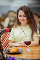 Beautiful dark-haired young curly woman sits in summer cafe and drinks coffee cocktail. Warm. Rest.