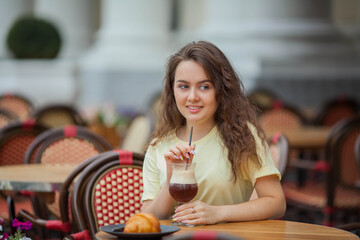 Beautiful dark-haired young curly woman sits in summer cafe and drinks coffee cocktail. Warm. Rest.