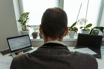  Back view of stock trader with raised hands looking at multiple computer screens with data and...