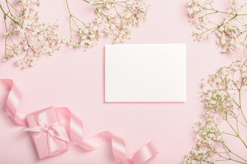 Flat lay composition with empty blank gift box, satin ribbon and gypsophila on pink background....