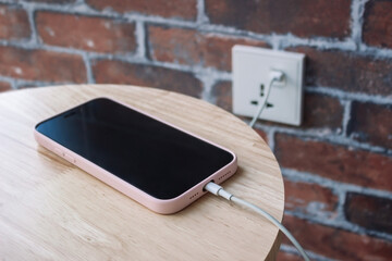 A mobile phone in a pink case charging battery by wire. A charging smartphone with cable on a...