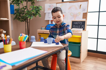 Adorable hispanic boy playing with toys sitting on table at kindergarten