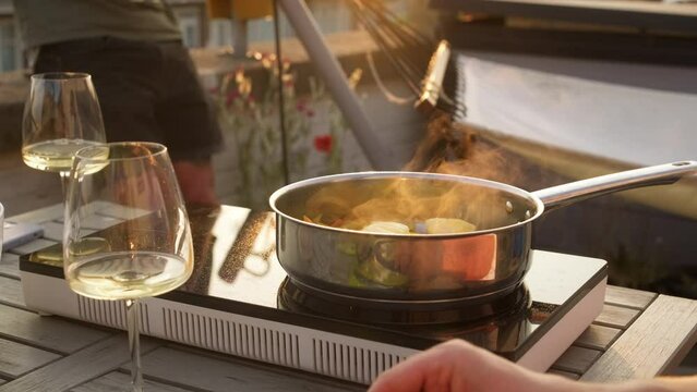 Summer party during sunset on a private outdoor terrace with wine and food. Cooking on a portable electric stove on the balcony of the apartment. Cozy joy time with family and friend