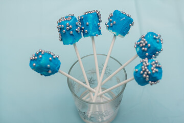 A photo of a glass containing 6 blue color lollypop or Popsicle with silver beads. this is a photo of edible popsicle or lollypop. 