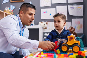 Hispanic man and boy playing with construction blocks and tractor toy at kindergarten