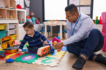 Hispanic man and boy playing with car toy sitting on floor at kindergarten