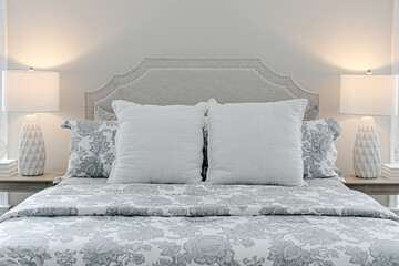 Beautiful neutral calm primary bedroom with large bed with pattern bedding and matching lamps white walls professionally styled