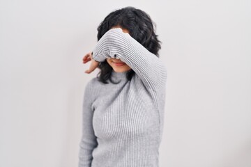 Hispanic woman with dark hair standing over isolated background covering eyes with arm, looking...
