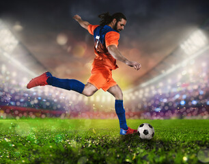 Soccer scene at night match with player in a orange uniform kicking the ball with power