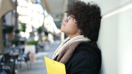 Young african american woman looking serious holding folder at street
