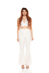 Fashion style studio portrait of beautiful young woman. White wide leg pants and white sleevles shirt. Model standing and posing against white background