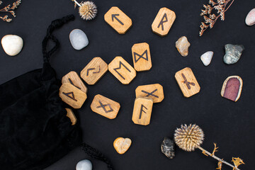 Black textile bag with stack of wooden runes and stones on a table. Scandinavian magical esoteric...