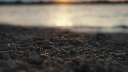 Ocean waves with sun reflection rolling on sand beach with small stones at sunset. Close-up of sea comb with ocean water splashes in twilight. Nature background. After sunset blue color.