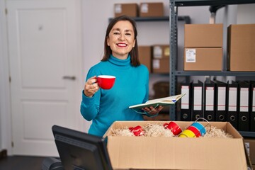 Middle age woman ecommerce business worker unpacking cardboard box at office
