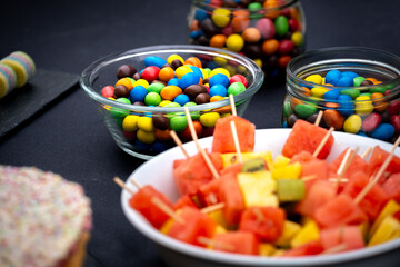 Pride month concept, gay symbol. Different colors slices of fruit and chocolates in a dark table.