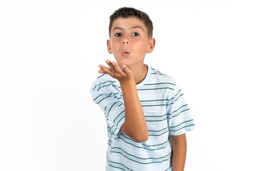 Little hispanic boy wearing  striped T-shirt  looking at the camera blowing a kiss with hand on air being lovely and sexy. Love expression.