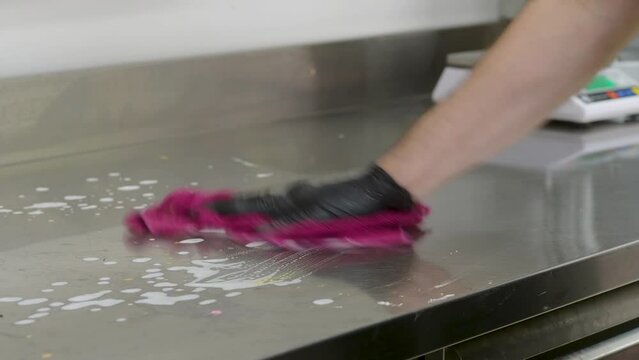 person weari g gloves cleaning a professional kitchen counter.