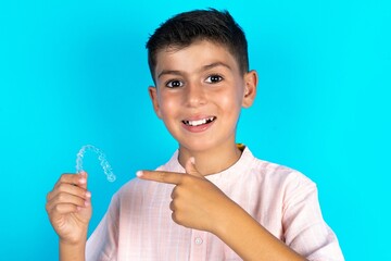 Little hispanic boy wearing white shirt  holding an invisible aligner and pointing at it. Dental...
