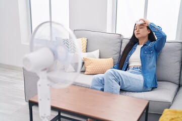 Young chinese woman using ventilator sitting on sofa at home